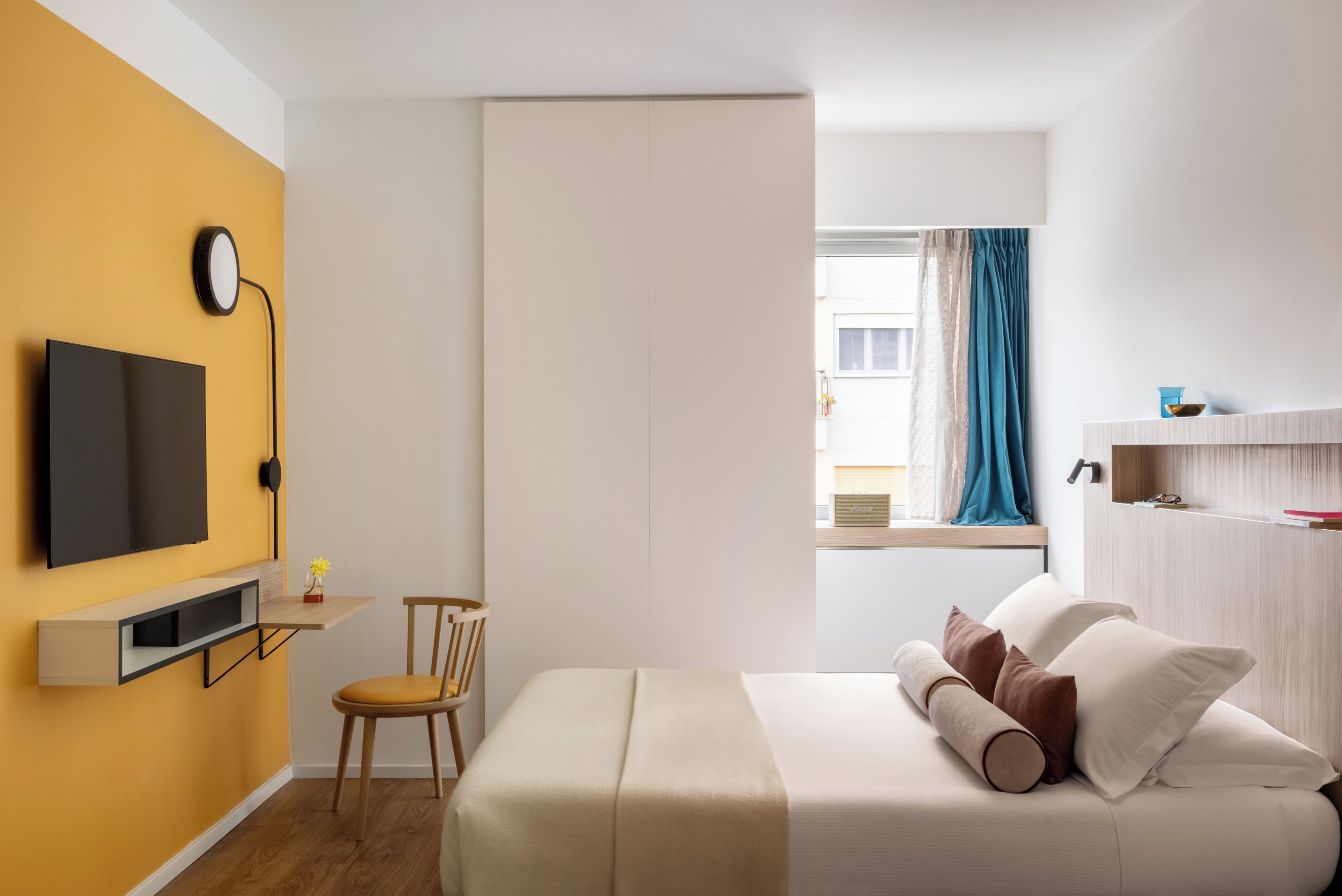 Un dormitorio moderno con cama, escritorio, silla, televisión y ventana con cortinas.