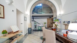 A spacious lobby with a high arched ceiling, a staircase leading to an upper level, a reception desk, and a seating area with a chair and a table. - Hotel Rivoli (Sorrento)