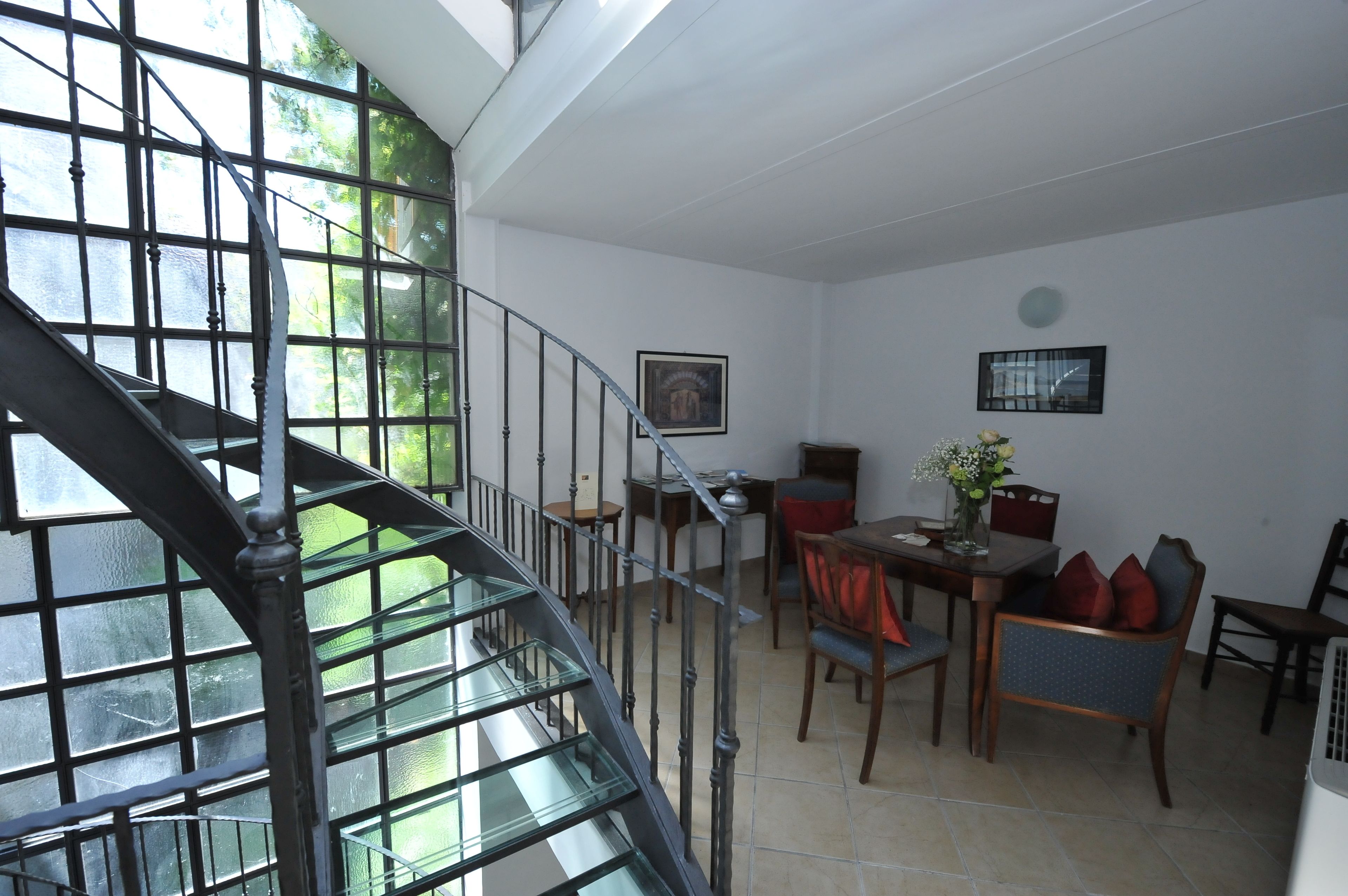 A dining area with a table and chairs, a staircase with glass railings, and a framed picture on the wall.