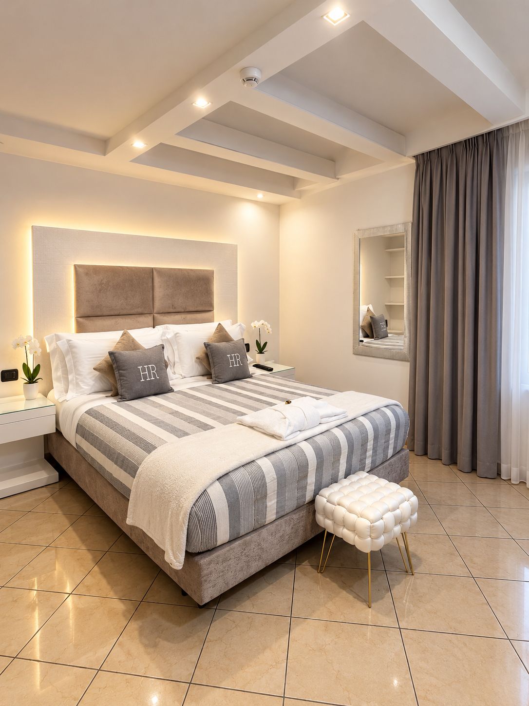 Un dormitorio moderno con una cama grande, mesitas de noche, un tocador, un espejo y una ventana con cortinas.
