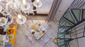A dining area with a table set for four, surrounded by clear chairs, and a staircase with glass railings. - Hotel Rivoli (Sorrento)
