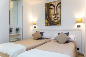 Habitación de hotel con dos camas, un cuadro grande de Buda y lámparas fijadas a la pared.