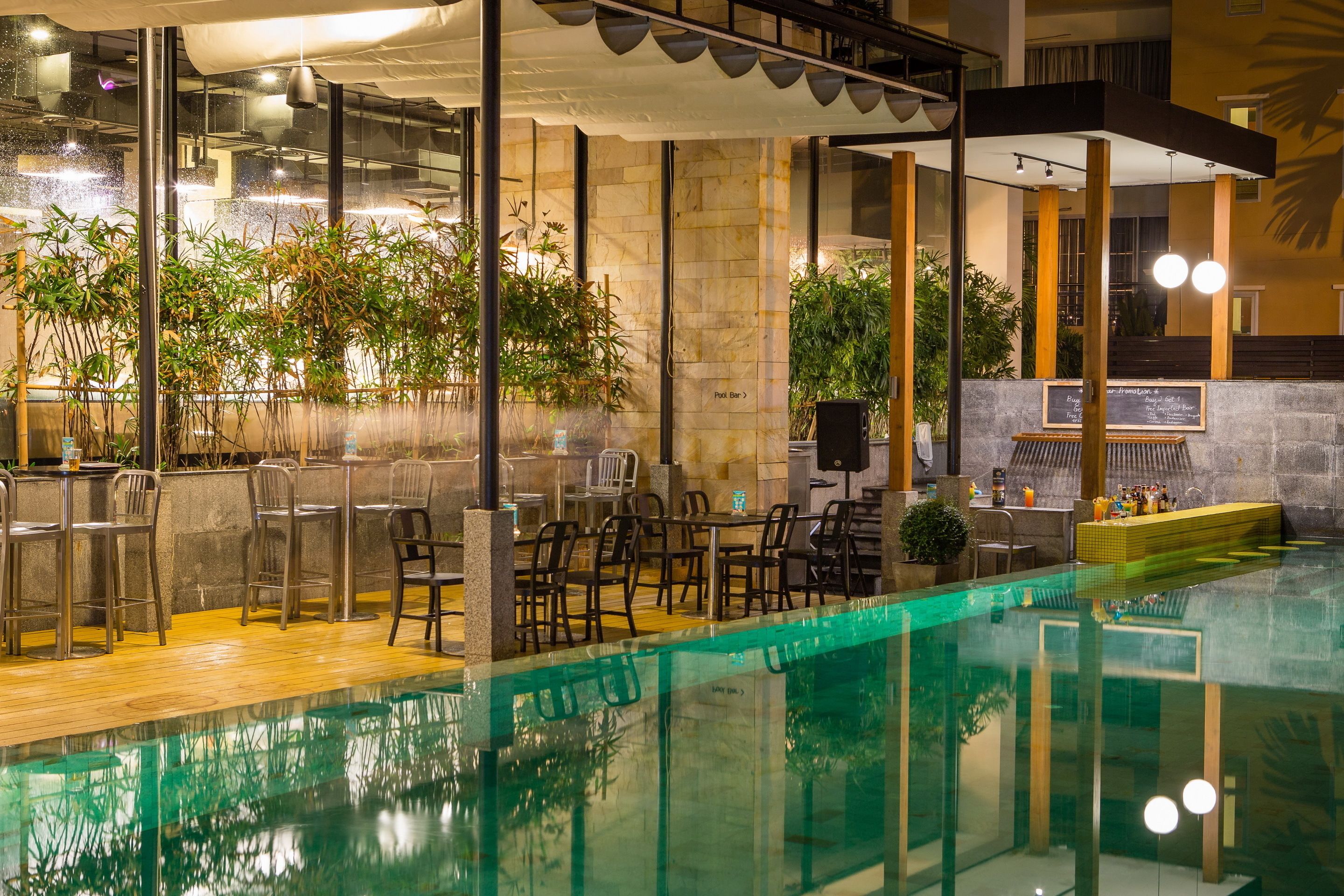 An indoor pool area with a bar and seating, surrounded by plants and a stone wall.