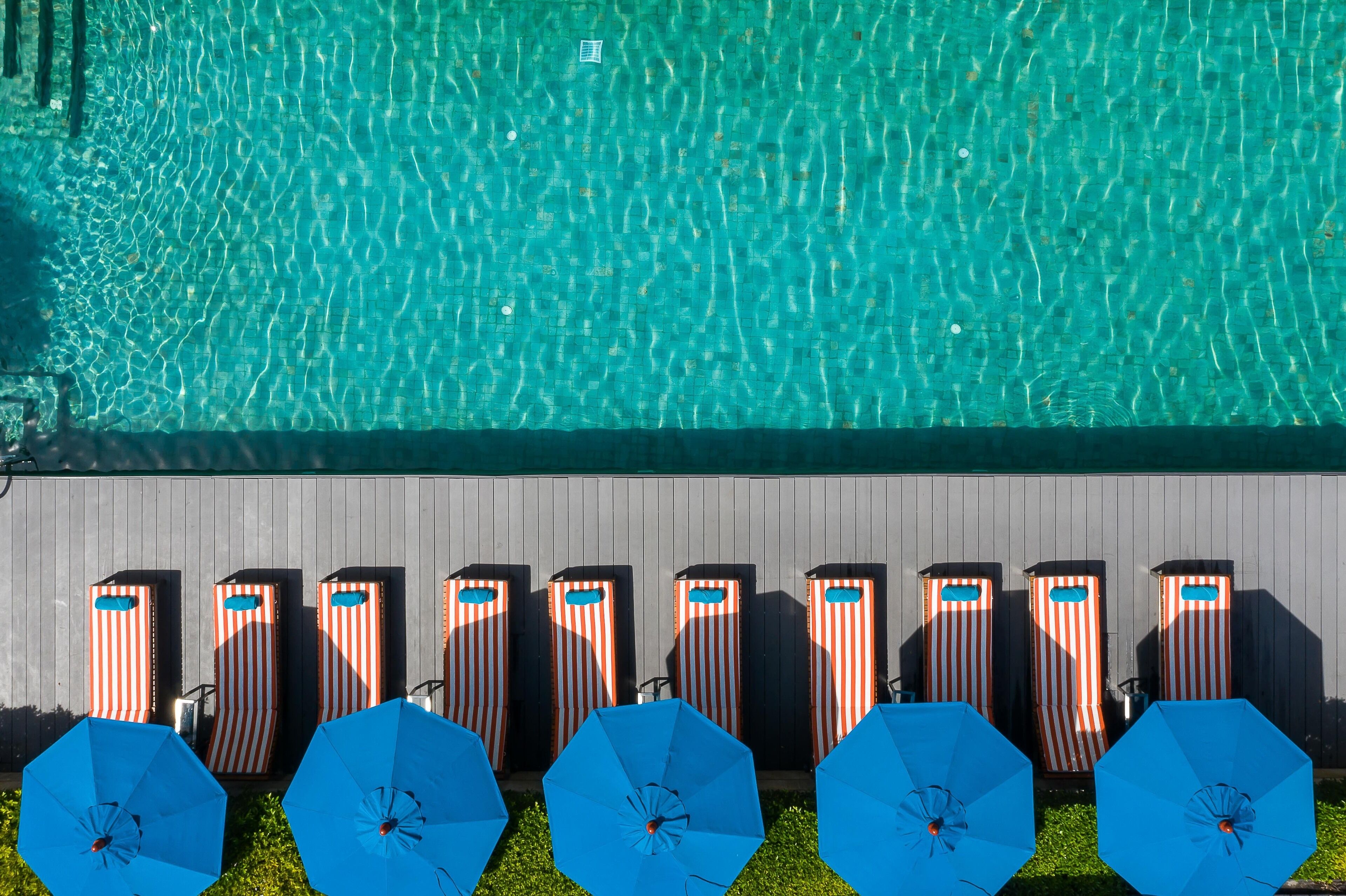 Une piscine à l’eau claire et un espace de détente avec des chaises longues à rayures et des parasols bleus.