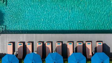 Une piscine à l’eau claire et un espace de détente avec des chaises longues à rayures et des parasols bleus.