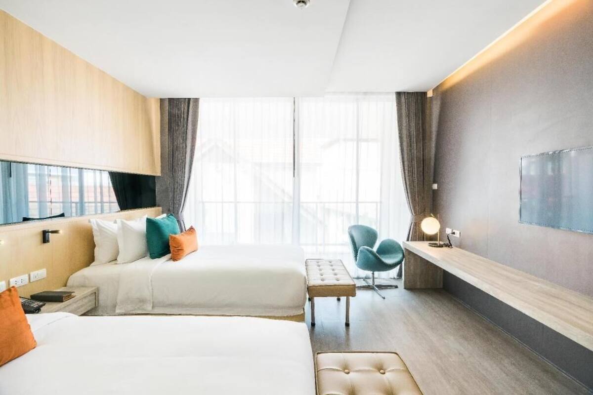 Ein Hotelzimmer mit zwei Betten, einem Schreibtisch, einem Stuhl und einem großen Fenster.