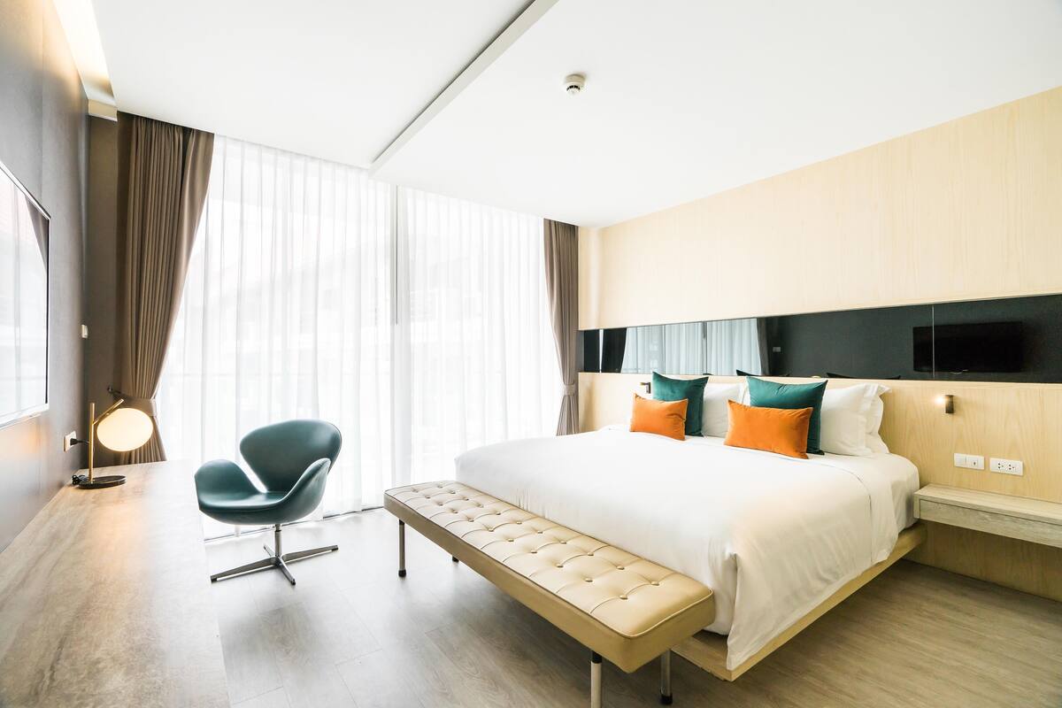 Ein modernes Hotelzimmer mit einem großen Bett, einer Bank, einem Sessel und einem Fernseher an der Wand.