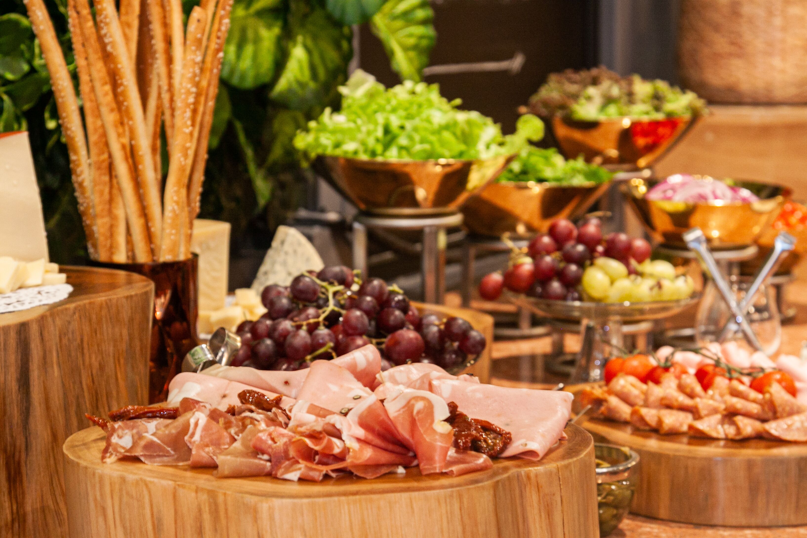 Variedad de quesos, embutidos y frutas sobre tablas de madera, sugiriendo un bufé o estación de comida.