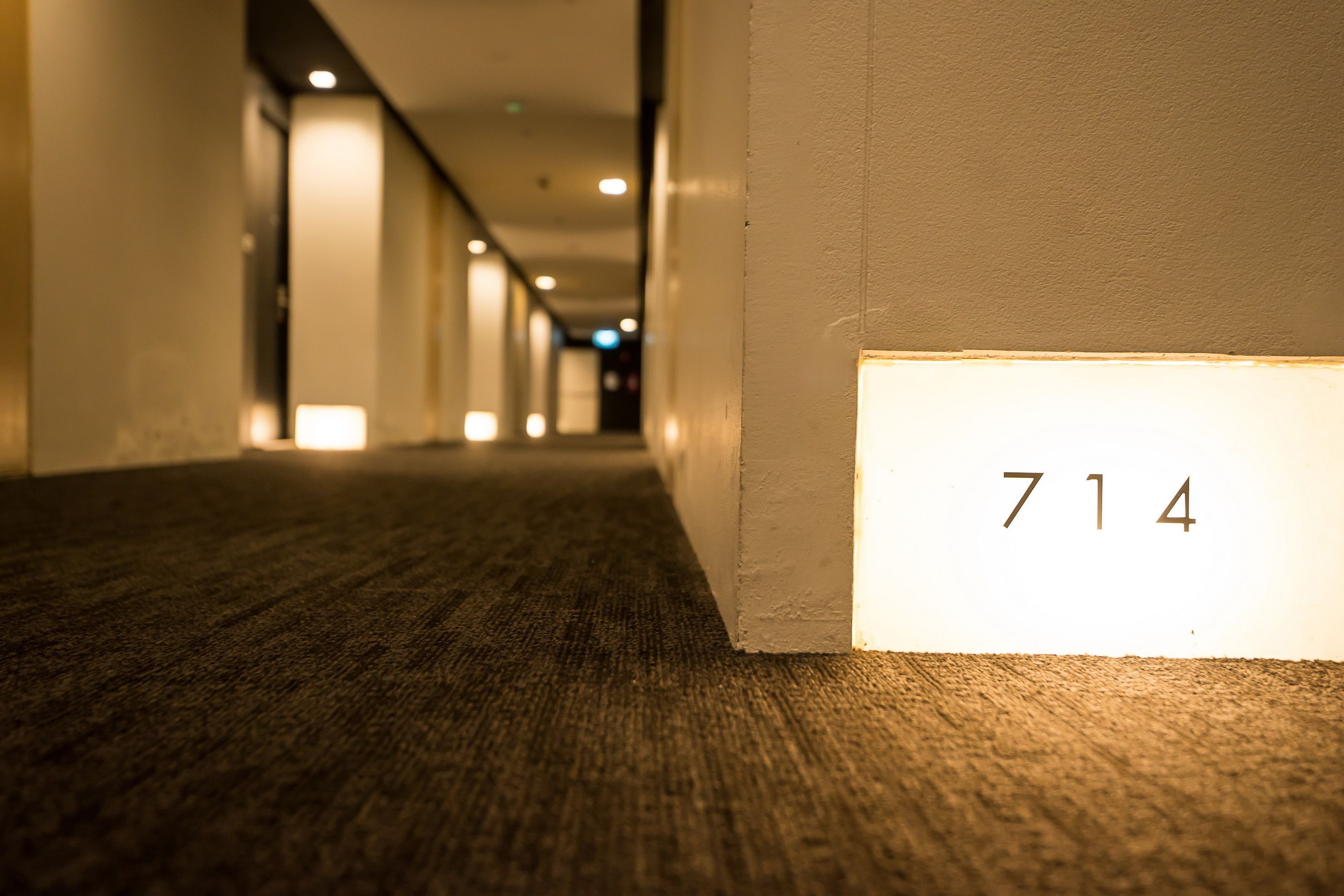 A corridor with a carpeted floor and a wall with the number 714 illuminated.