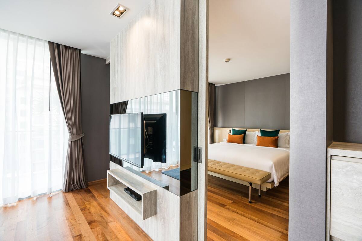 Ein modernes Hotelzimmer mit einem großen Flachbildfernseher, einem Bett mit vielen Kissen und Holzboden.