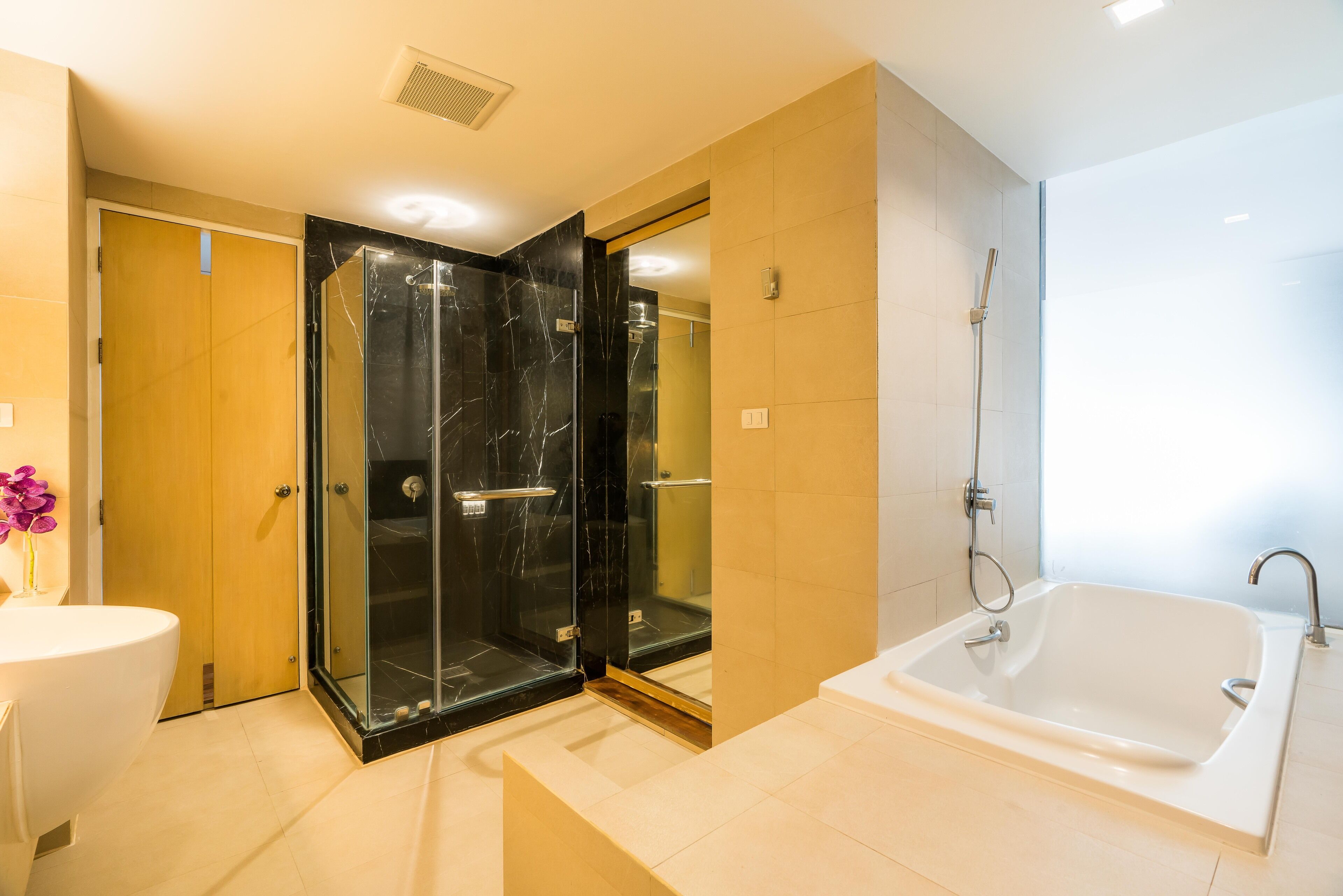 A modern bathroom with a glass-enclosed shower, a white bathtub, and a wooden door.