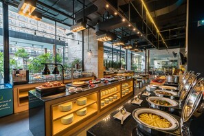 A buffet area with various food stations, a coffee machine, and a view of the cityscape through large windows.