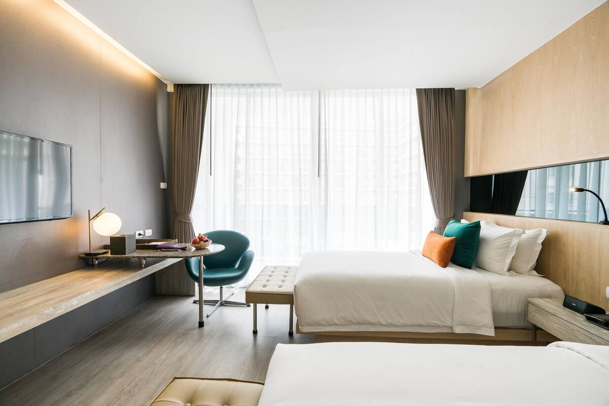 Ein modernes Hotelzimmer mit einem großen Bett, einem Schreibtisch mit Lampe, einem Sessel und einem an der Wand montierten Fernseher.