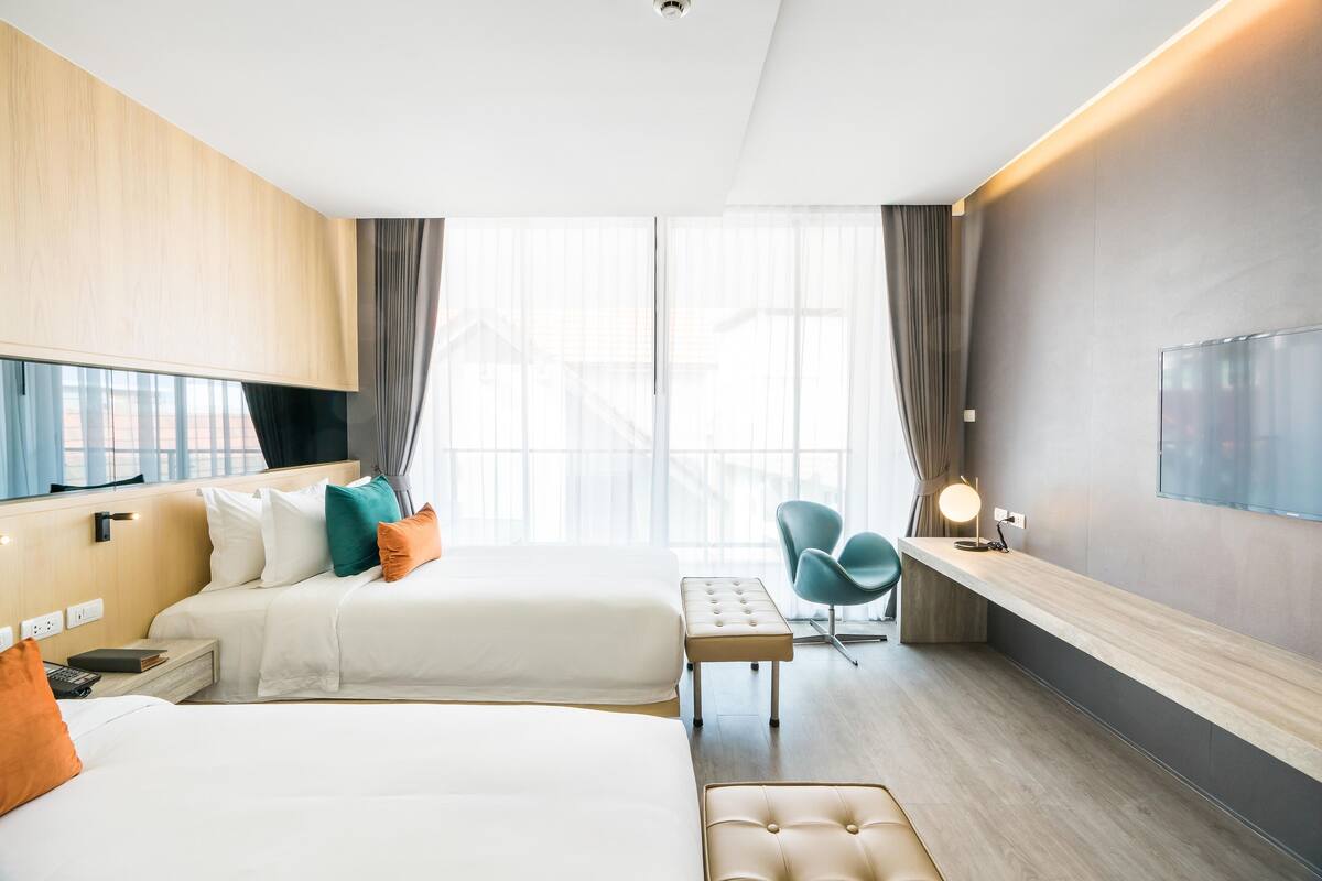 Ein modernes Hotelzimmer mit zwei Betten, einem Schreibtisch, einem Stuhl und einem Fernseher.