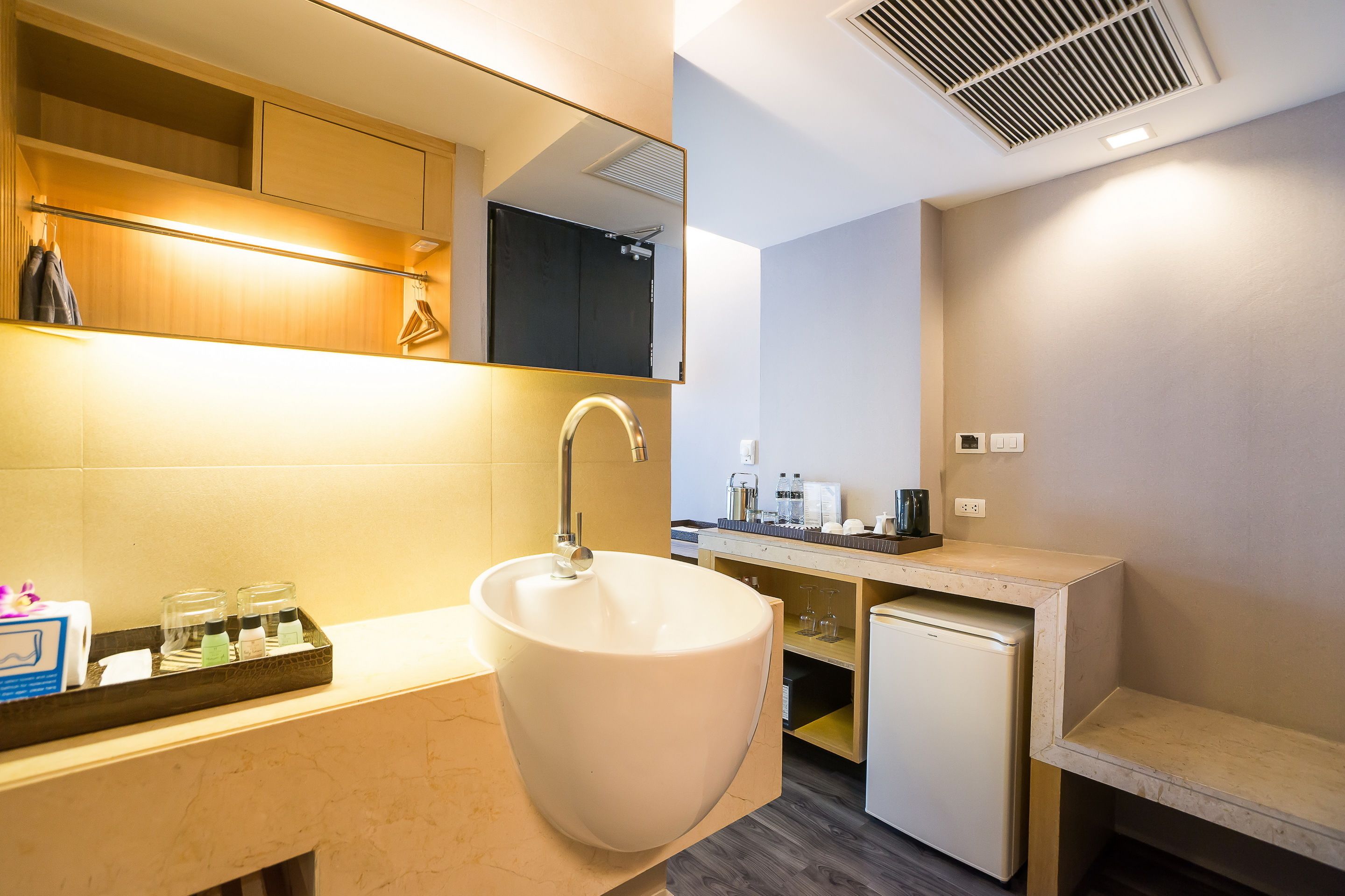 A modern bathroom with a large sink, a mirror, and a small refrigerator.
