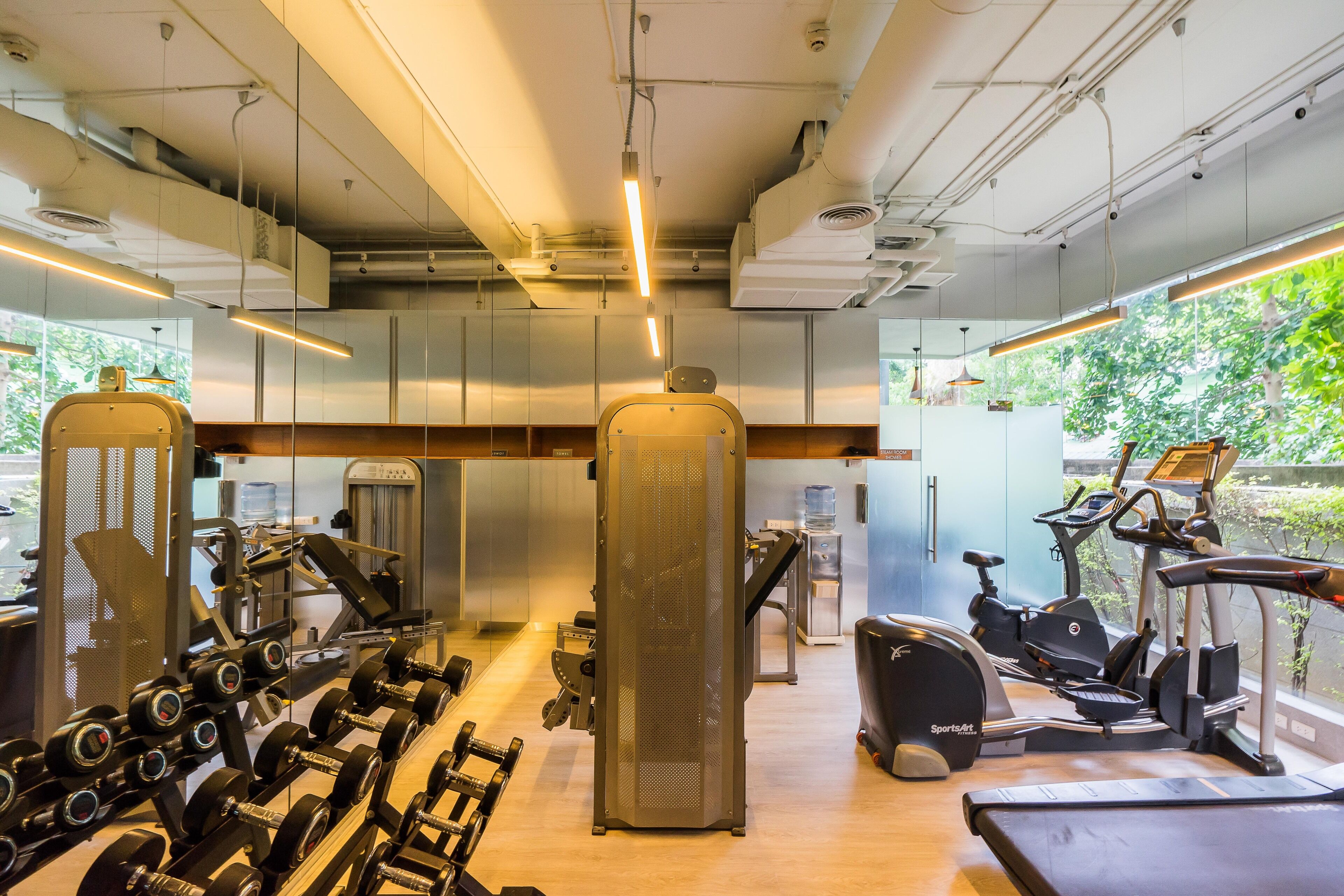 Un gimnasio con equipo de ejercicio, un dispensador de agua y vistas a zonas verdes.