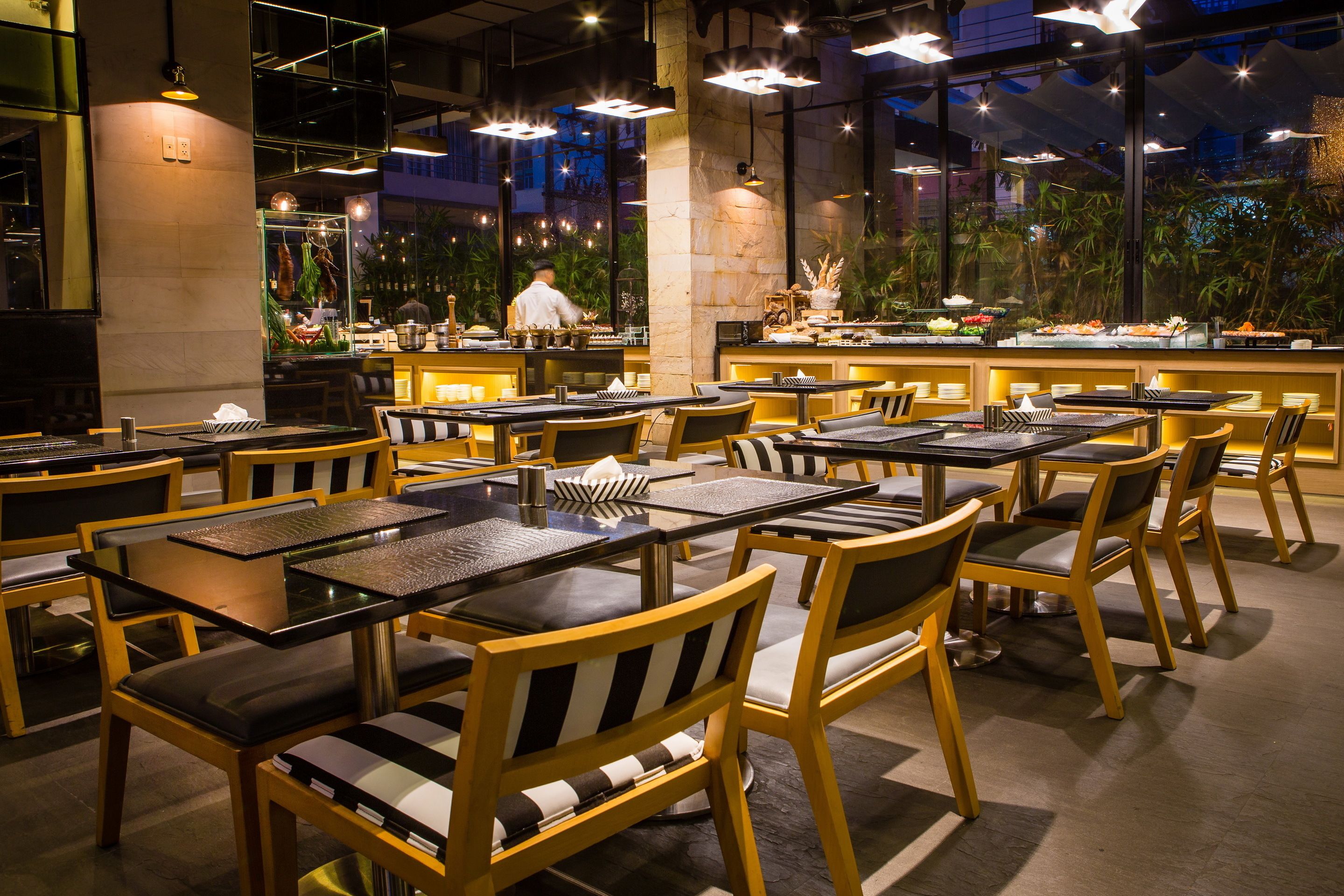 A restaurant with multiple tables and chairs, a chef preparing food, and a buffet area.