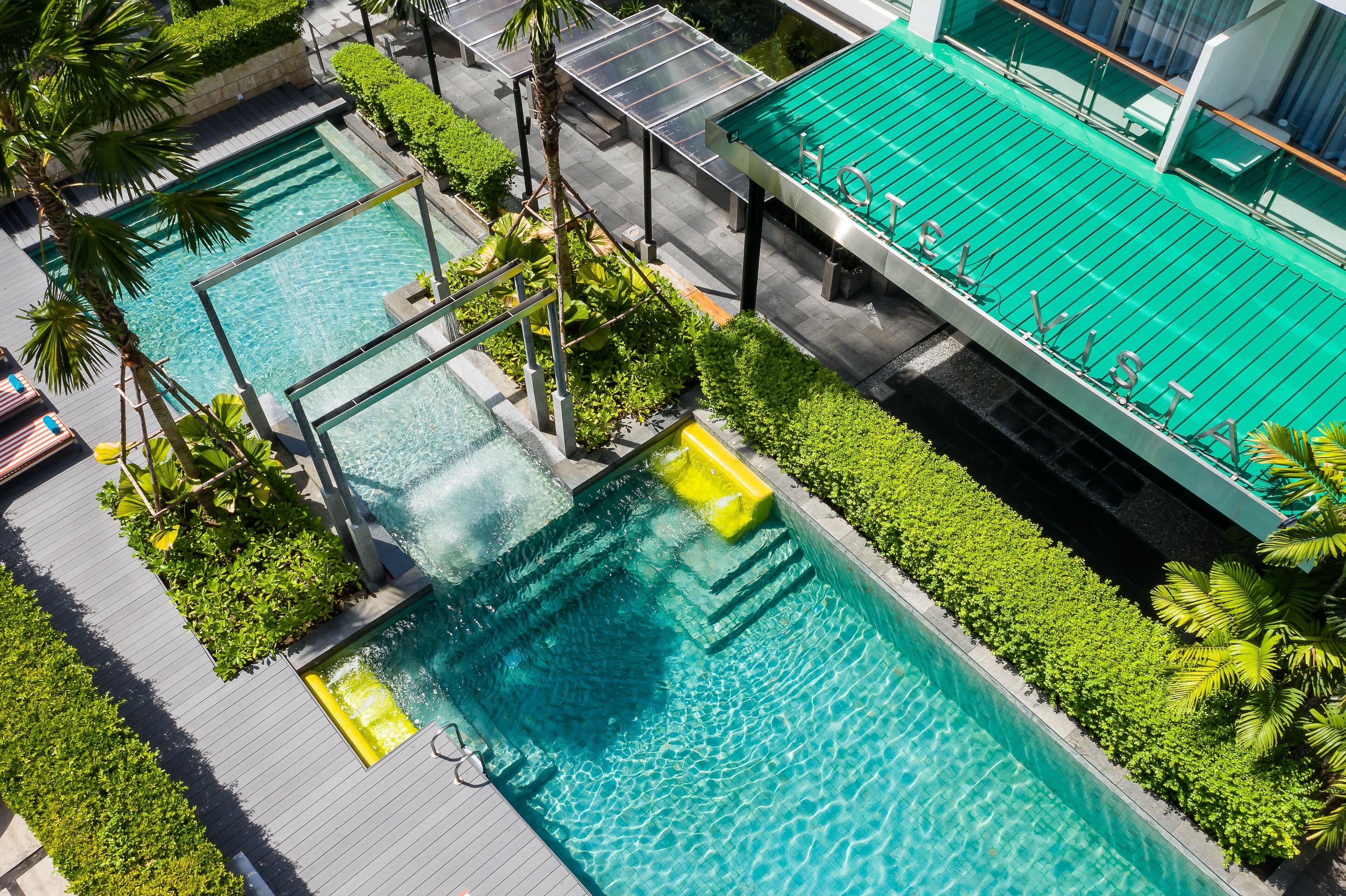 A rooftop pool with clear blue water, surrounded by greenery and a modern building structure.