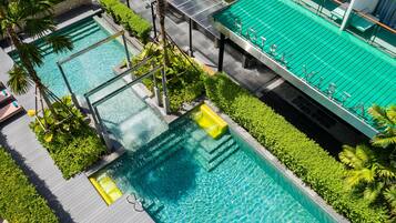 A rooftop pool with clear blue water, surrounded by greenery and a modern building structure.