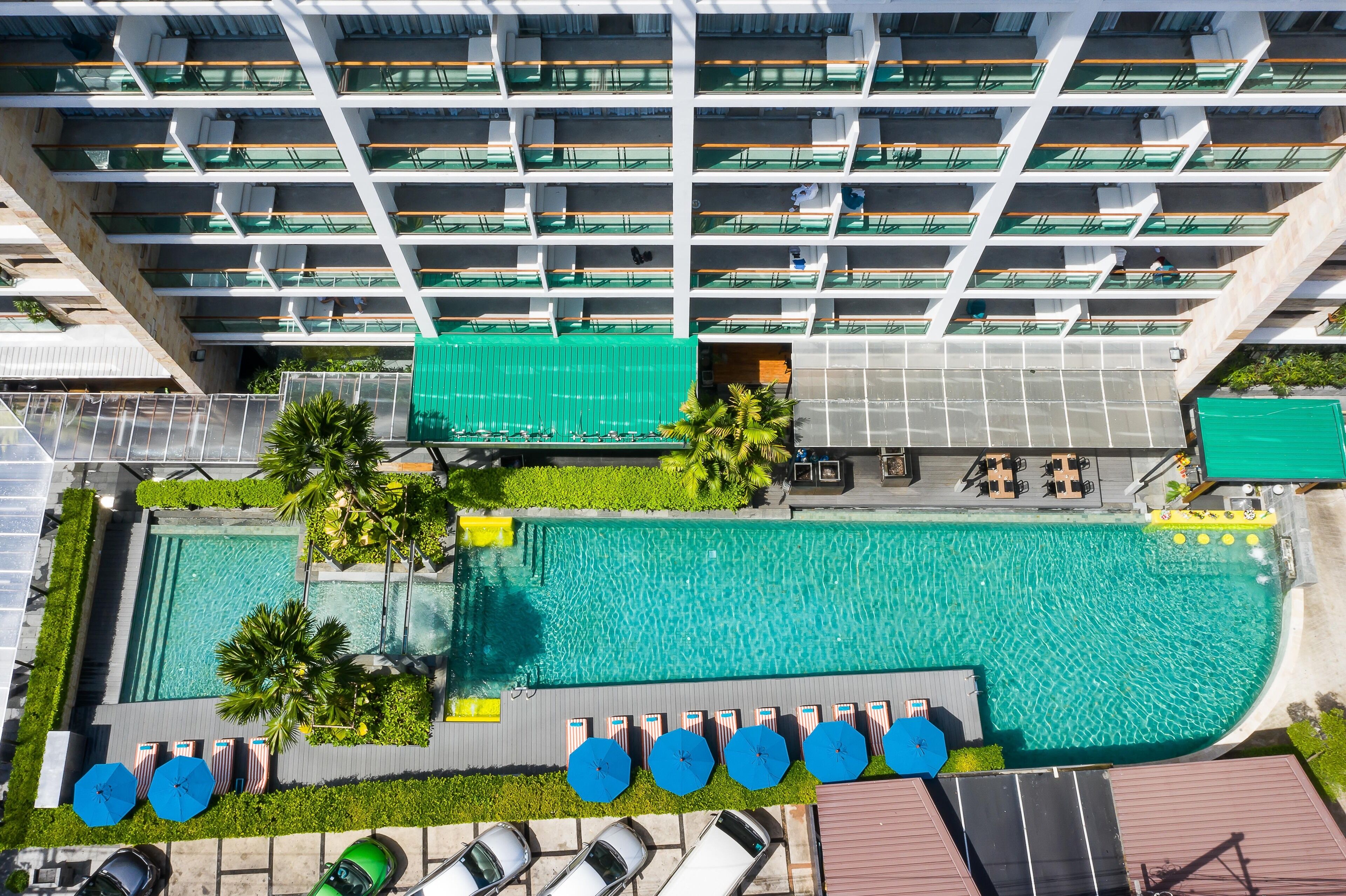 A high-rise hotel with multiple balconies, a central swimming pool, and outdoor seating areas.