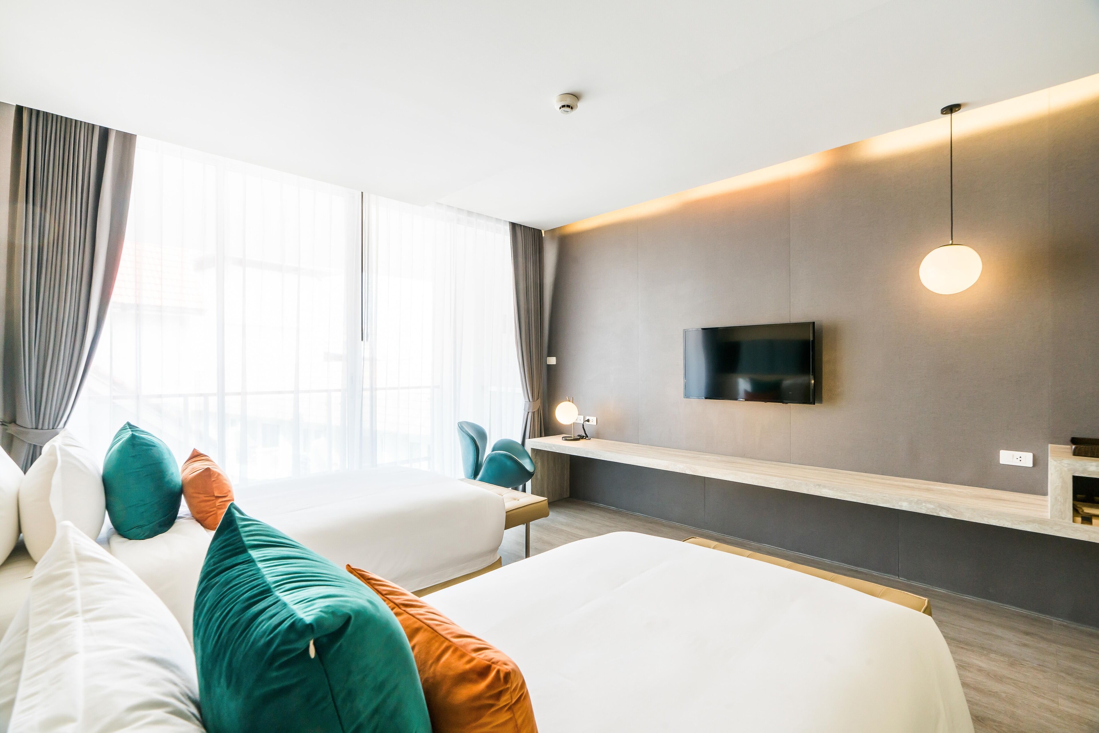 Une chambre d’hôtel moderne équipée de deux lits, d’une télévision, d’un bureau et d’une grande fenêtre avec des rideaux.