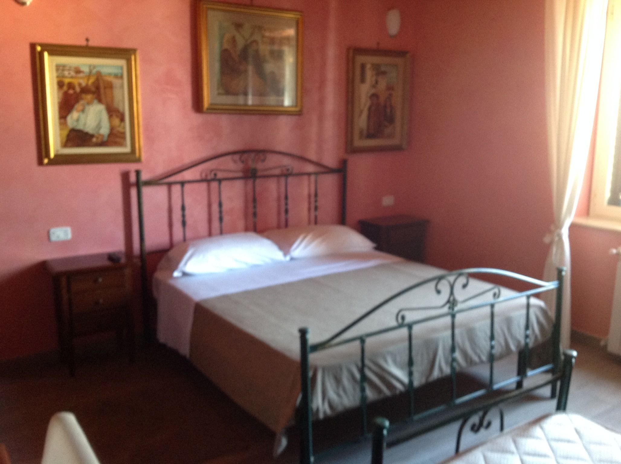 A bedroom with a metal bed frame, a bedside table, and a nightstand. There are three framed pictures on the wall.