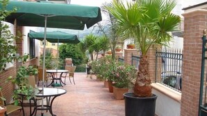 A patio area with tables and chairs, surrounded by potted plants and a green umbrella. - Villa Scotillo 1950 (Agropoli)