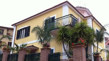 A two-story house with a yellow facade, black shutters, and a balcony with a wrought iron railing.