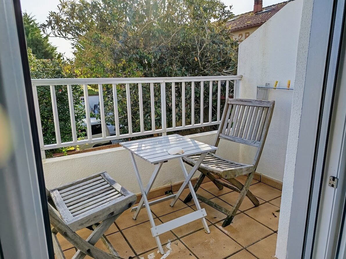 A balcony with a white railing, a small table, and two wooden chairs.