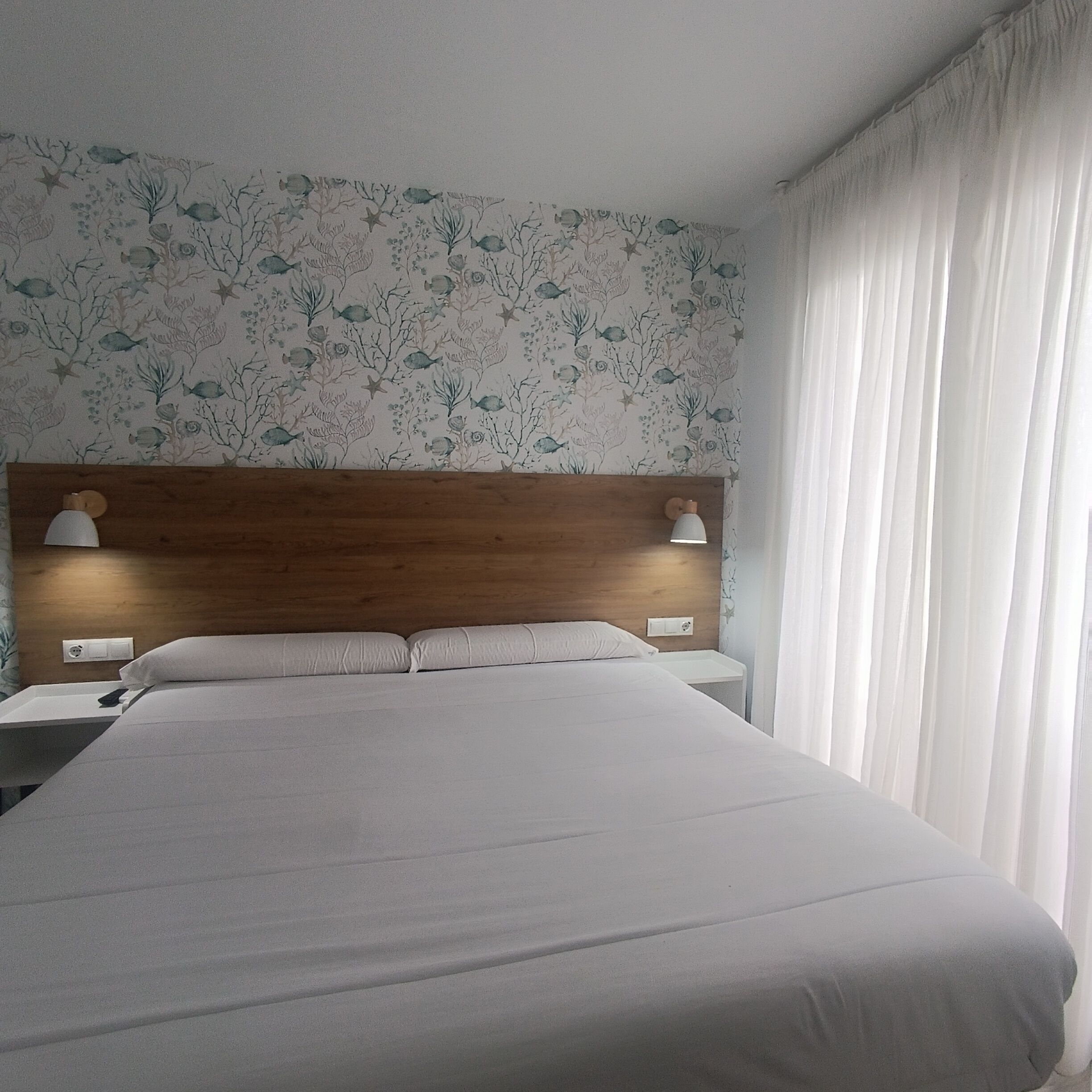 A hotel room with a large bed, two bedside tables with lamps, a wooden headboard, and a floral wallpaper.