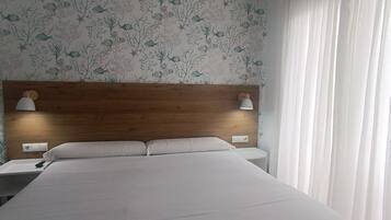 A hotel room with a large bed, two bedside tables with lamps, a wooden headboard, and a floral wallpaper.
