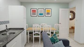 Una cocina compacta con comedor, armarios blancos, encimera de granito y una mesa con sillas. Hay tres obras de arte enmarcadas en la pared sobre la mesa.