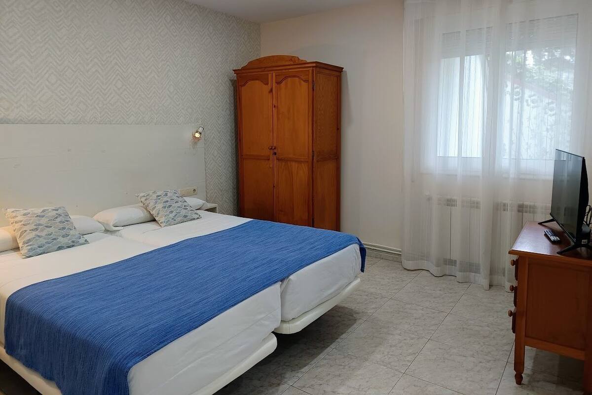 A bedroom with a bed, a wardrobe, a TV stand, and a window with curtains.