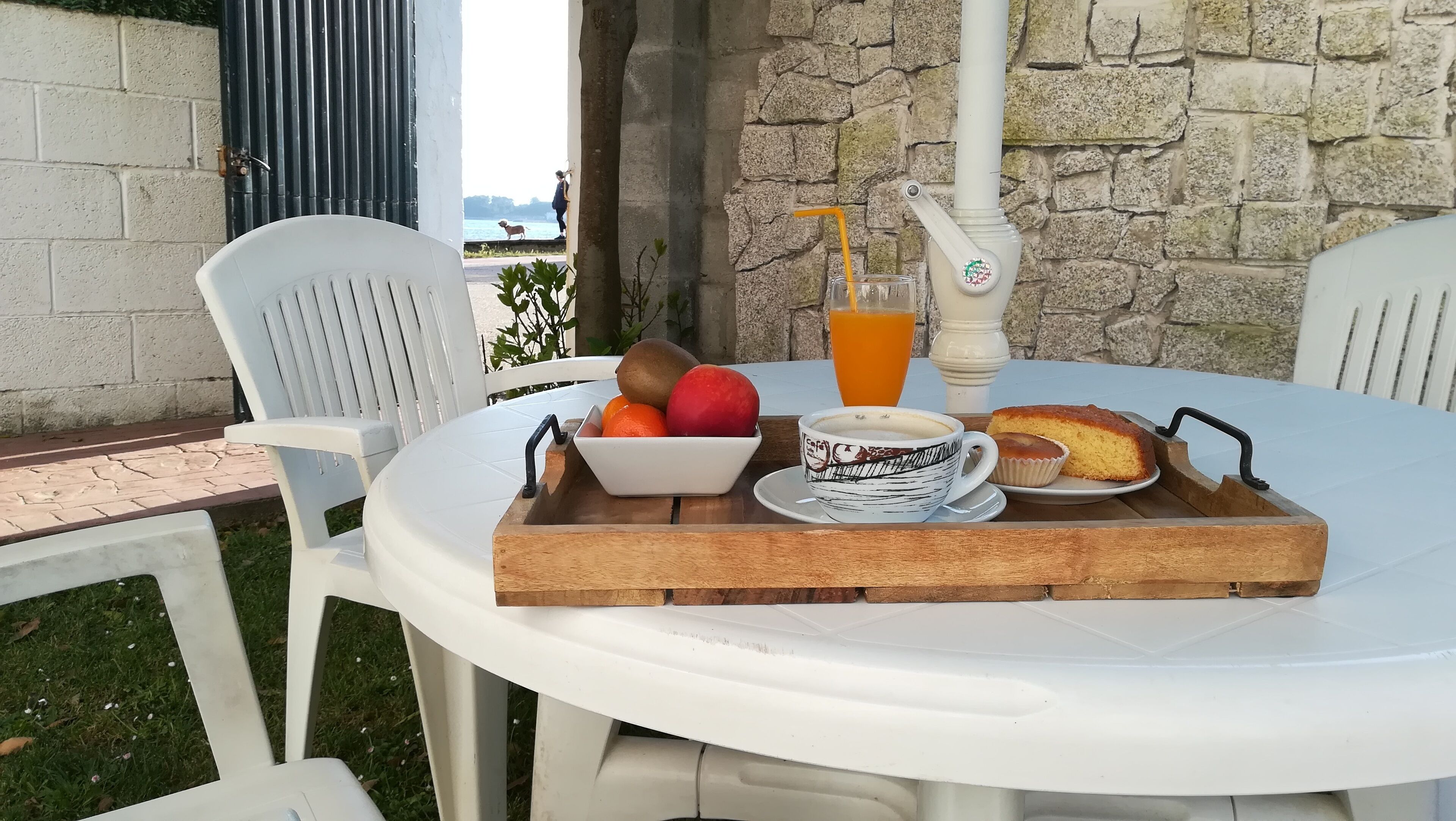 A table set with breakfast items including a bowl of fruit, a cup of coffee, a glass of orange juice, and a slice of cake.