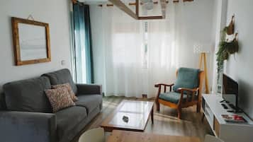 Sala de estar com sofá cinzento, mesa de centro de madeira, poltrona de madeira e aparador com monitor.