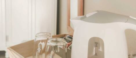 A white electric kettle on a tray with two glasses and a packet of tea.