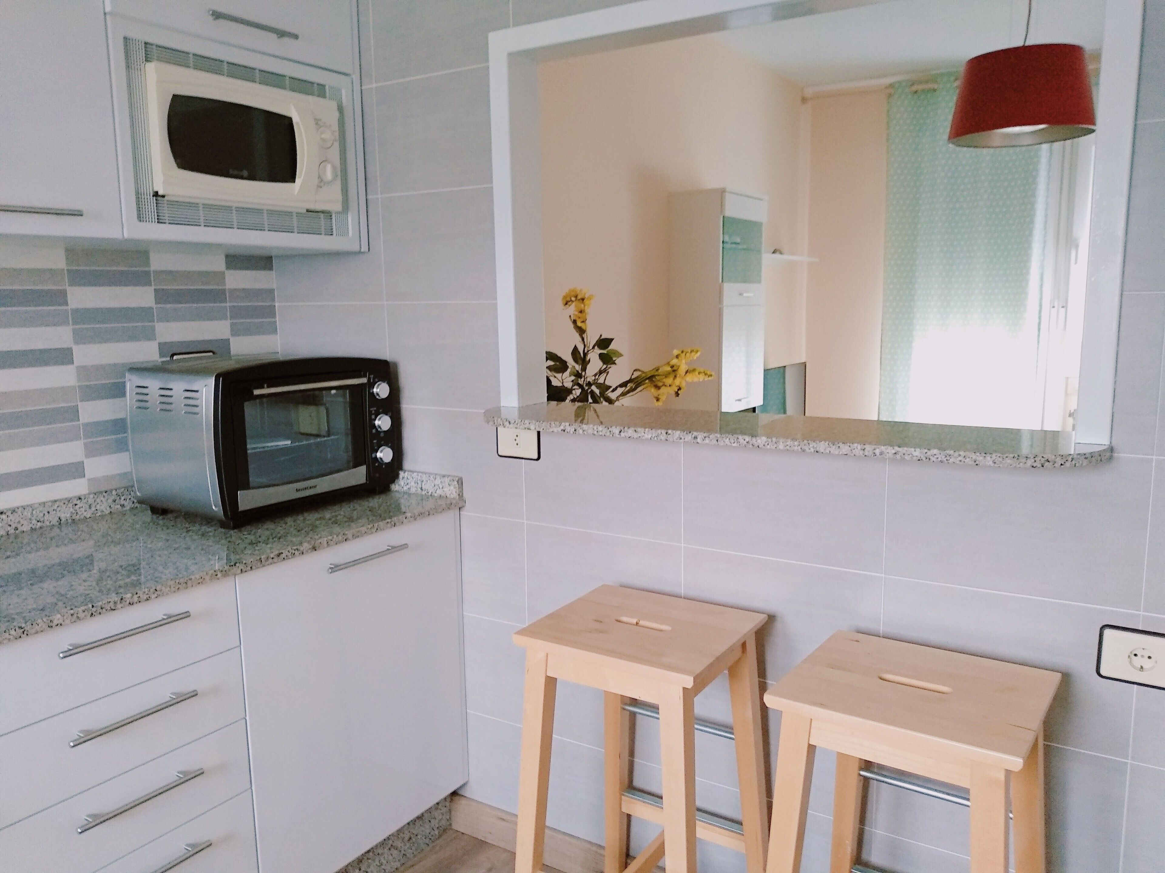 Una cocina con microondas, tostadora y dos taburetes de madera.