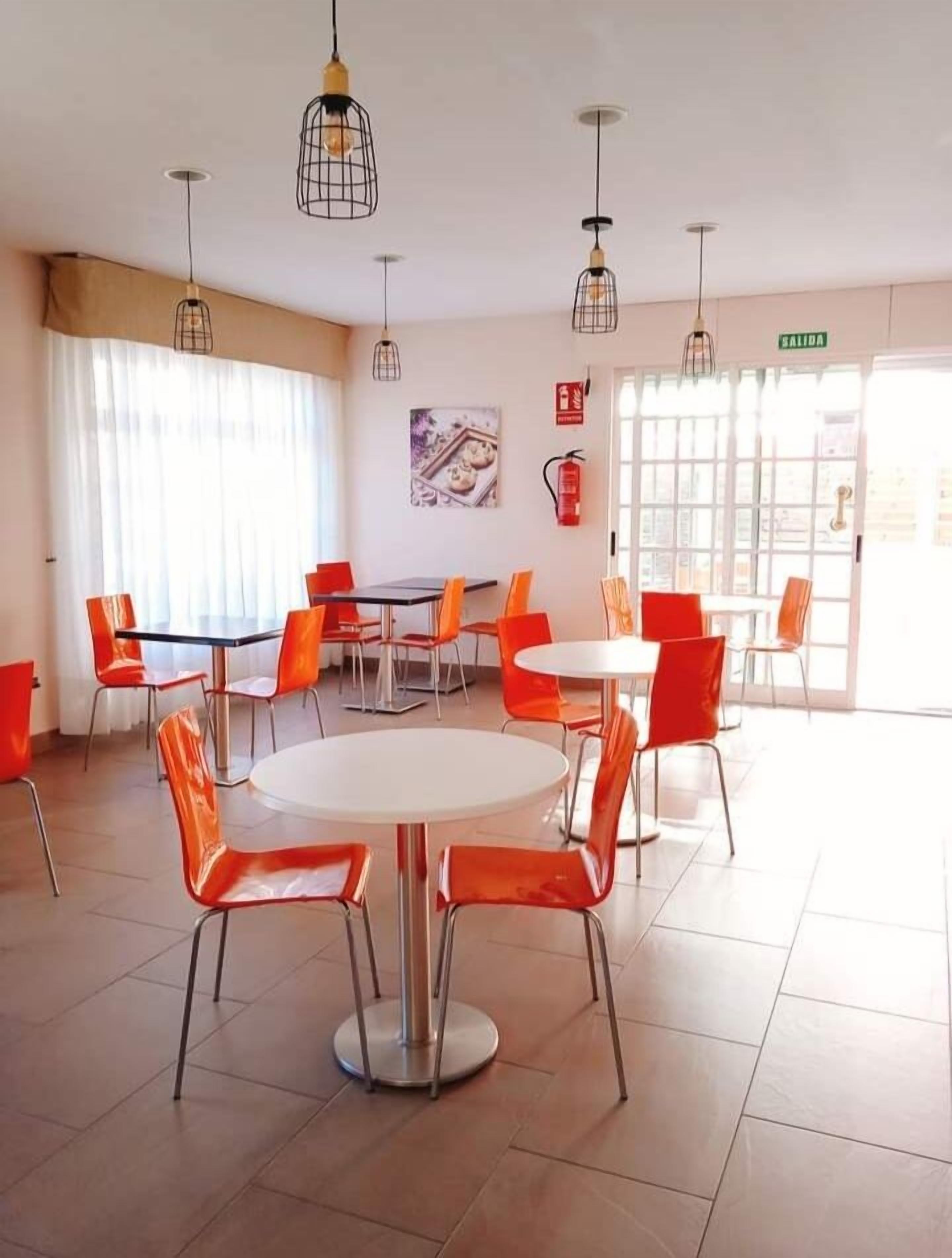 A dining area with round tables and orange chairs, a fire extinguisher, and a 'SALIDA' sign.