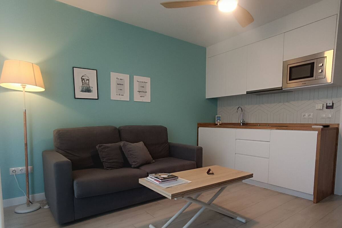 A living room with a sofa, a coffee table, a lamp, and a kitchen area with a microwave.