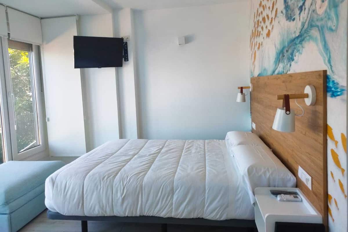 A modern bedroom with a large bed, a mounted TV, and a wooden headboard with a lamp.