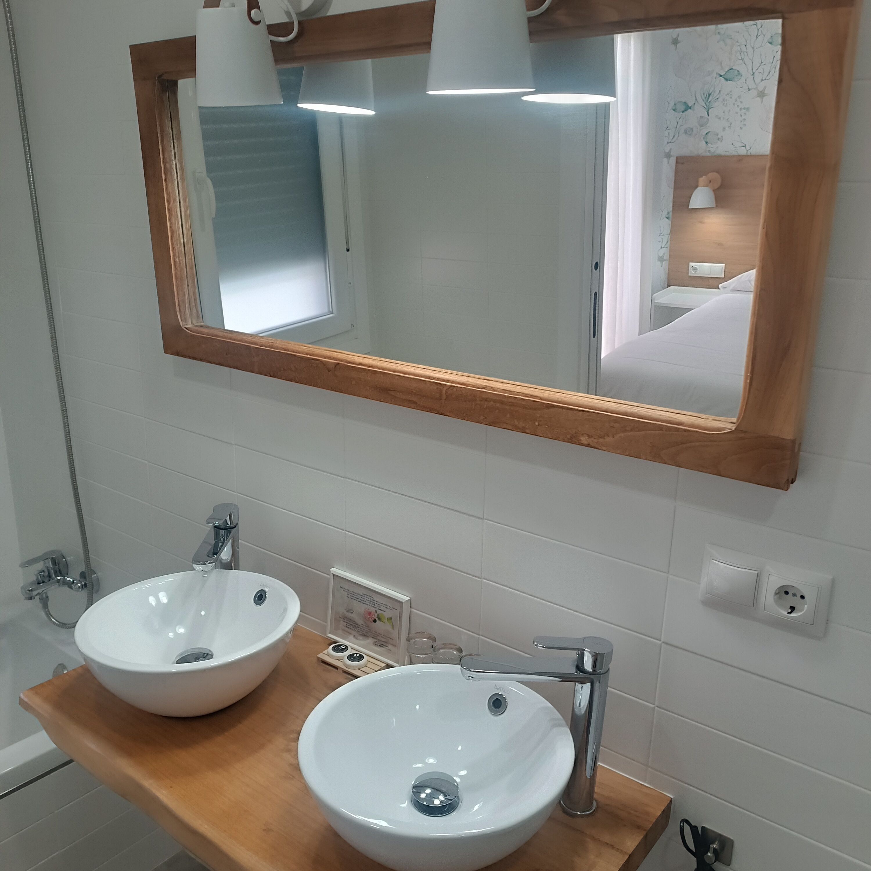 Un baño con dos lavamanos blancos, una encimera de madera, un espejo con marco de madera y una zona de ducha.
