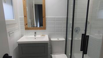 Un baño con un lavamanos blanco, un espejo con marco de madera, un inodoro y una cabina de ducha con paredes de vidrio.