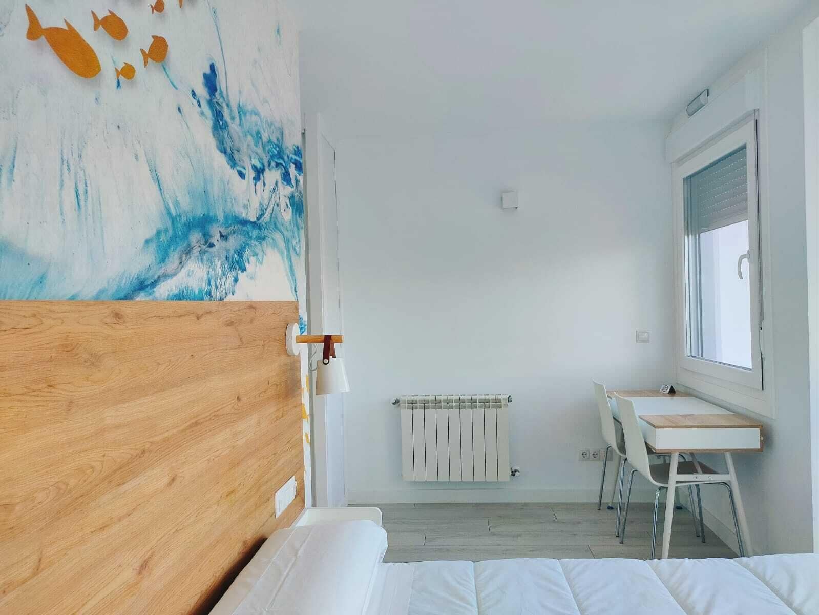 Een slaapkamer met een houten hoofdeinde, een bed, een bureau met stoel, een radiator en een raam.