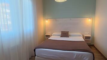 Une chambre à coucher avec un lit, deux tables de chevet, un luminaire suspendu et une fenêtre avec des rideaux.