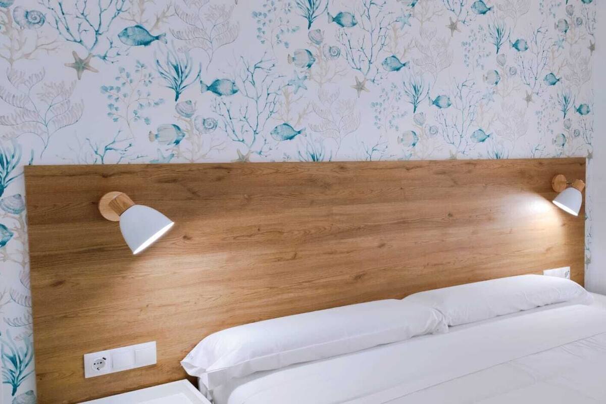 A bed with a wooden headboard, two bedside lamps, and a floral wallpaper pattern.