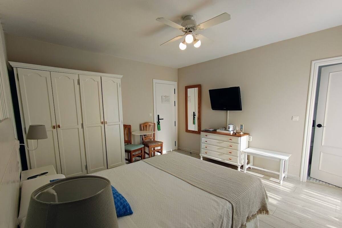 A bedroom with a bed, wardrobe, desk, chair, and a ceiling fan.
