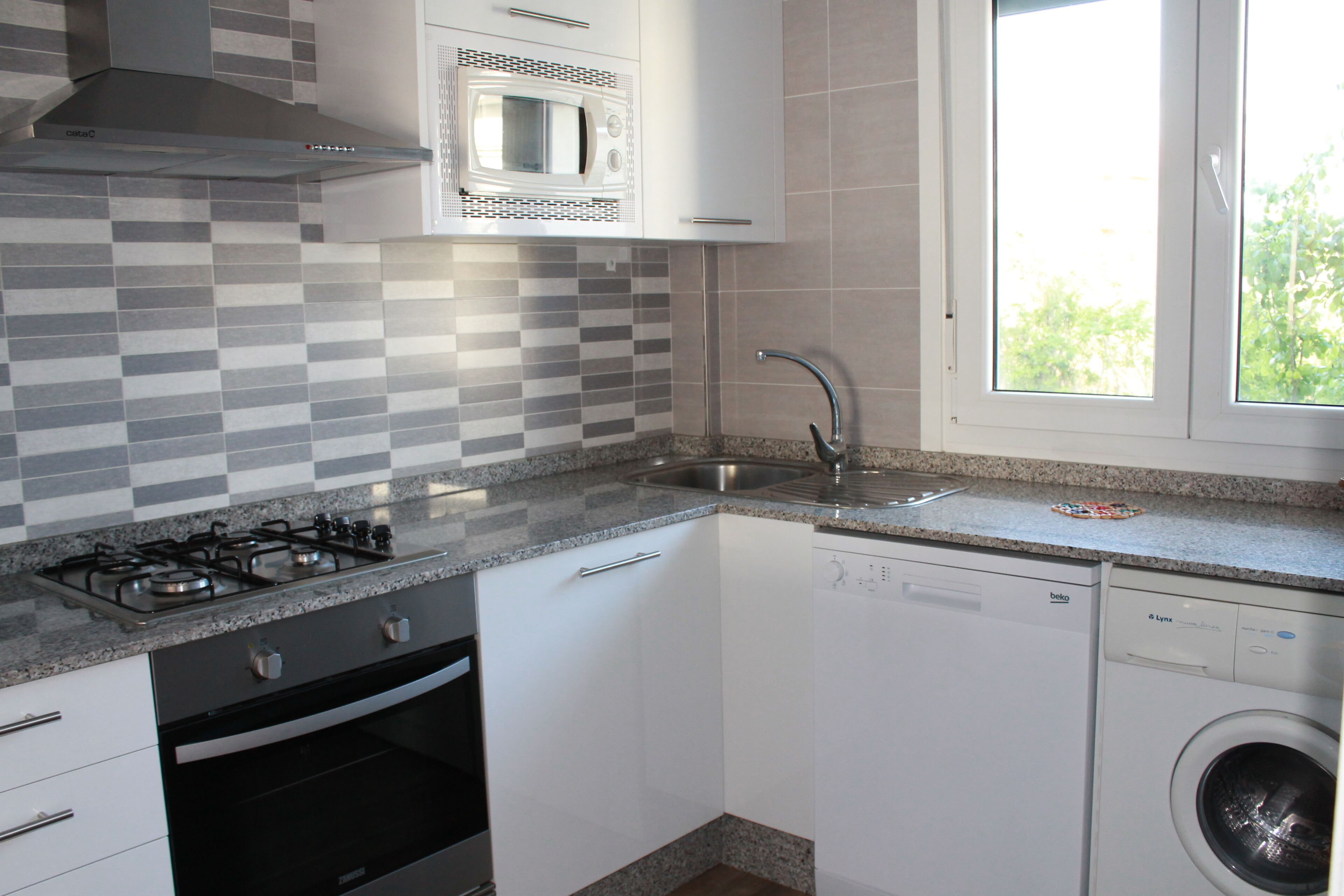 A compact kitchen with a gas stove, microwave, dishwasher, and a window with a view of greenery.