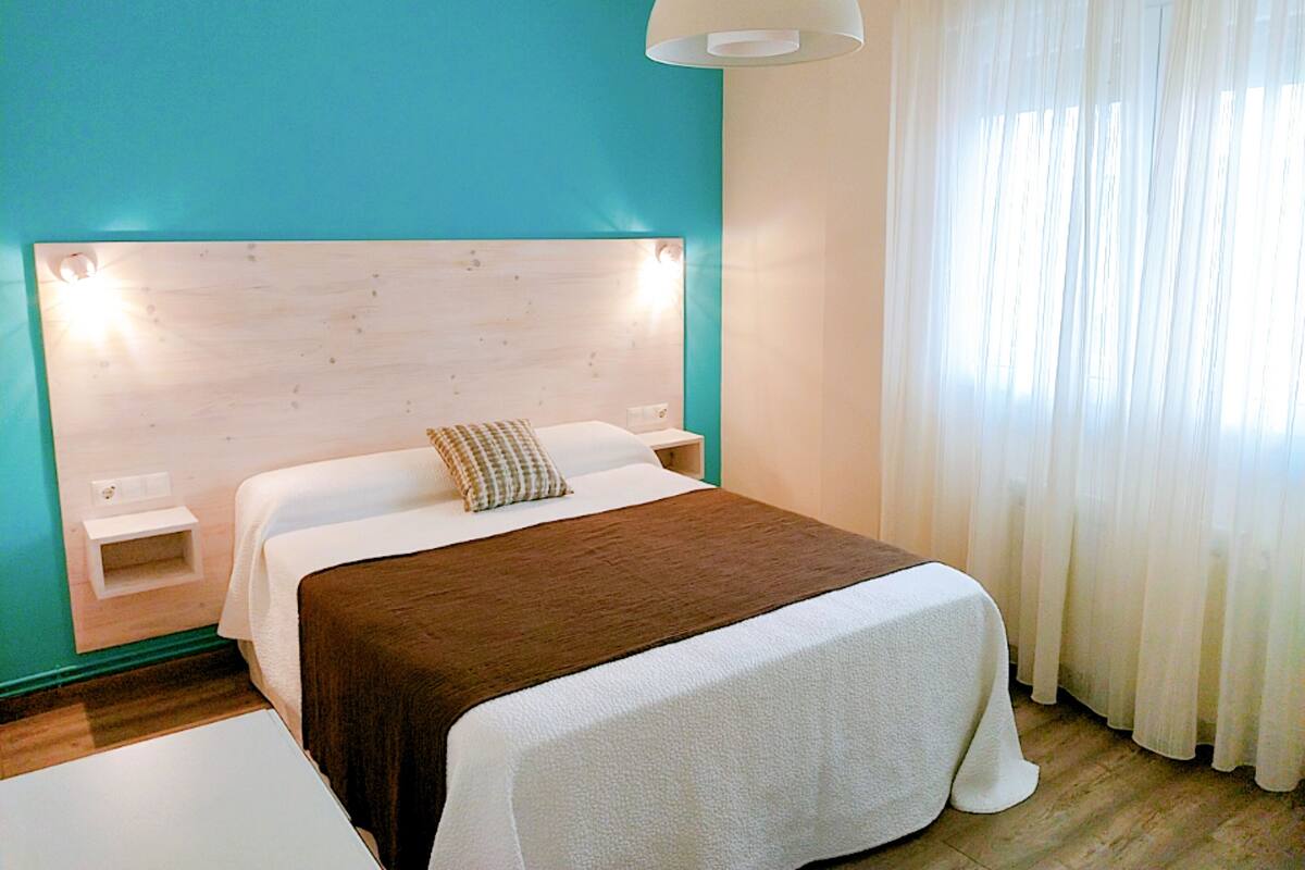 A hotel room with a wooden headboard, a large bed with a brown blanket, a bedside table, and a white lamp.