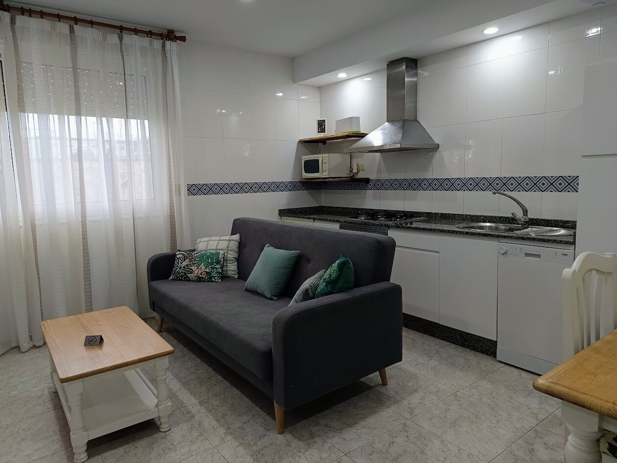Un ambiente compatto con divano, un piccolo tavolo, angolo cottura con forno a microonde ed elettrodomestici.