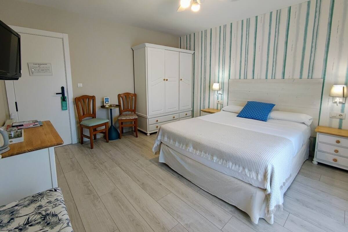 A bedroom with a bed, a wardrobe, a desk with a chair, and a television.